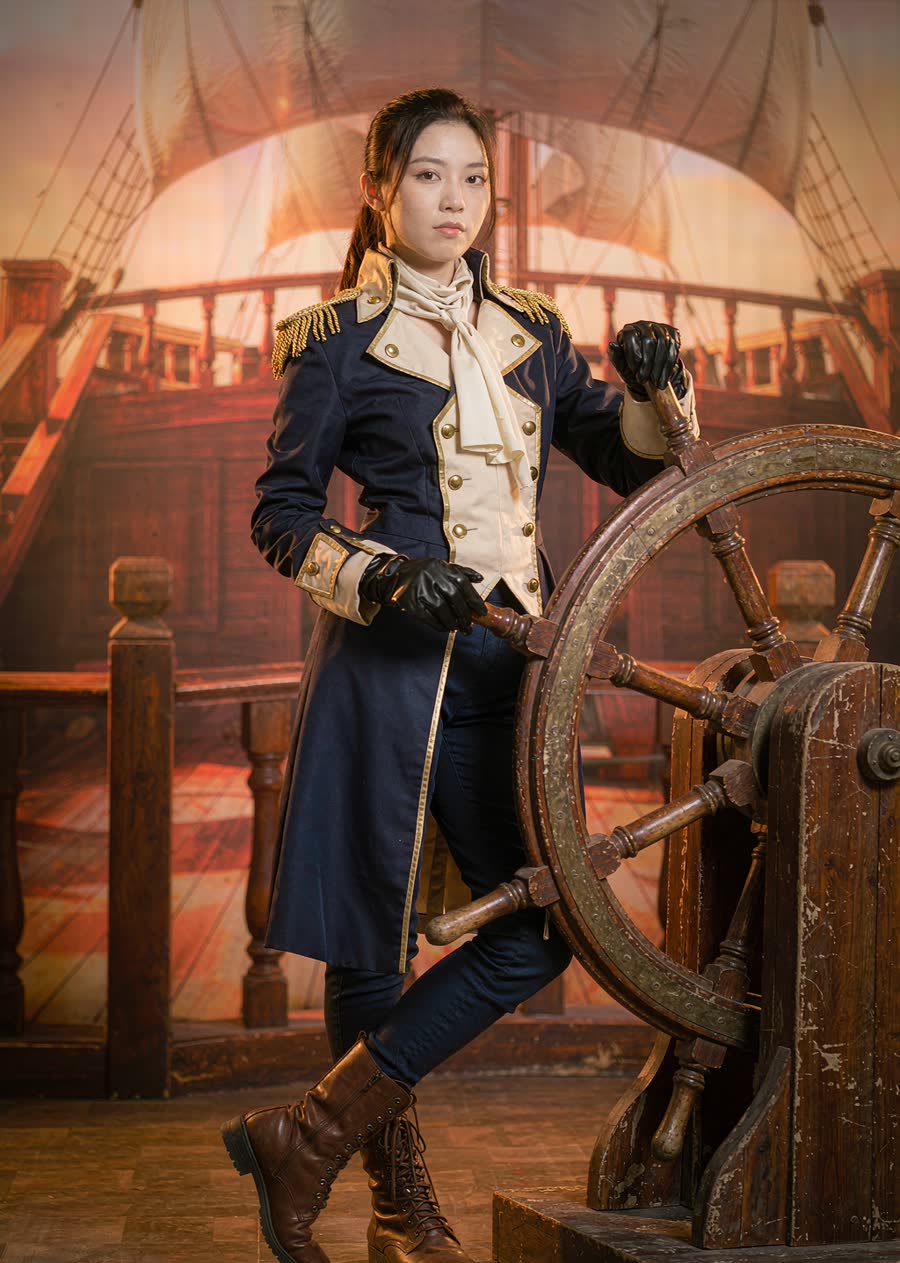 A woman in a weathered naval officer outfit with brass buttons and gold epaulettes, leaning against a ship's wheel prop, golden-hour sky with sunlit sails behind.